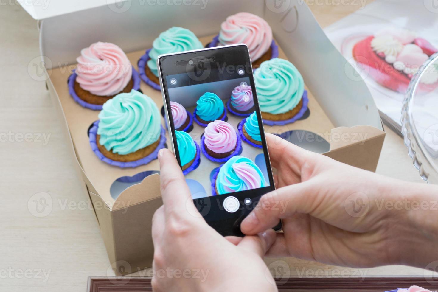 photographing a box with cupcakes with a phone by women's hands photo
