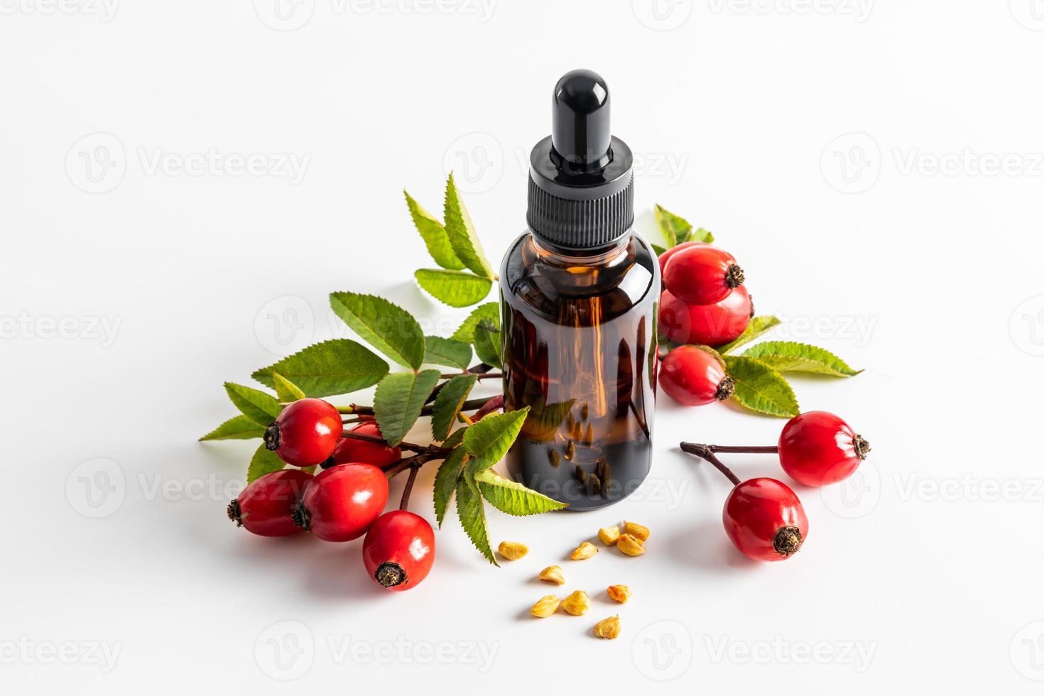 serum based on rosehip seed oil for facial skin care in a cosmetic bottle on a white background among ripe rosehip berries. moistening. nutrition. photo
