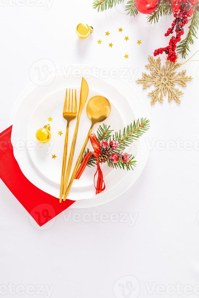 Vertical view of a set of white plates, gold fork, spoon, knife, red napkin on a white tablecloth. Christmas decorations. festive serving . photo
