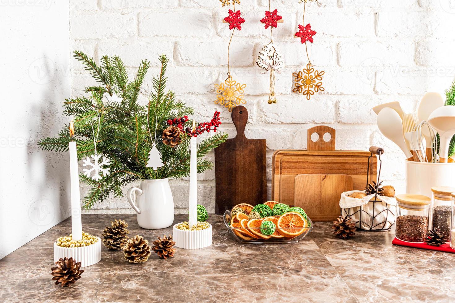 un fragmento de una parte de una cocina moderna con varias decoraciones navideñas, velas, un plato de rodajas de naranja secas. mesa de mármol. pared de ladrillo. foto