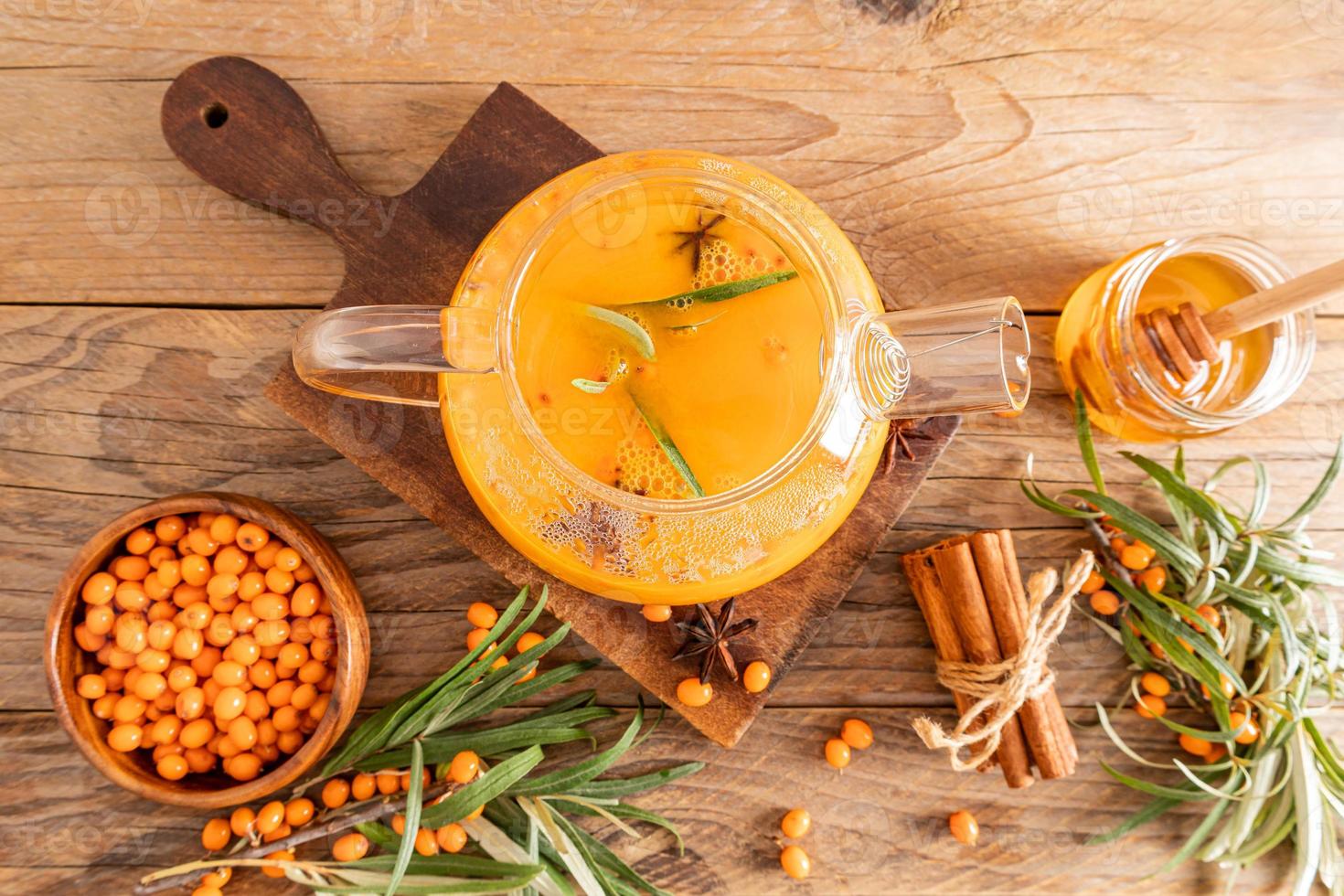 autumn composition of the tea ceremony. a large glass teapot with sea buckthorn tea, honey in a jar, berries in the bowl. top view. wooden background. photo