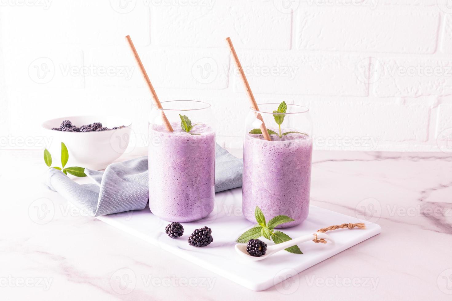 cóctel de bayas de mora o batido en vasos de vidrio modernos en forma de lata de cerveza con paja ecológica frente a una pared de ladrillo blanco. alimentación saludable. foto