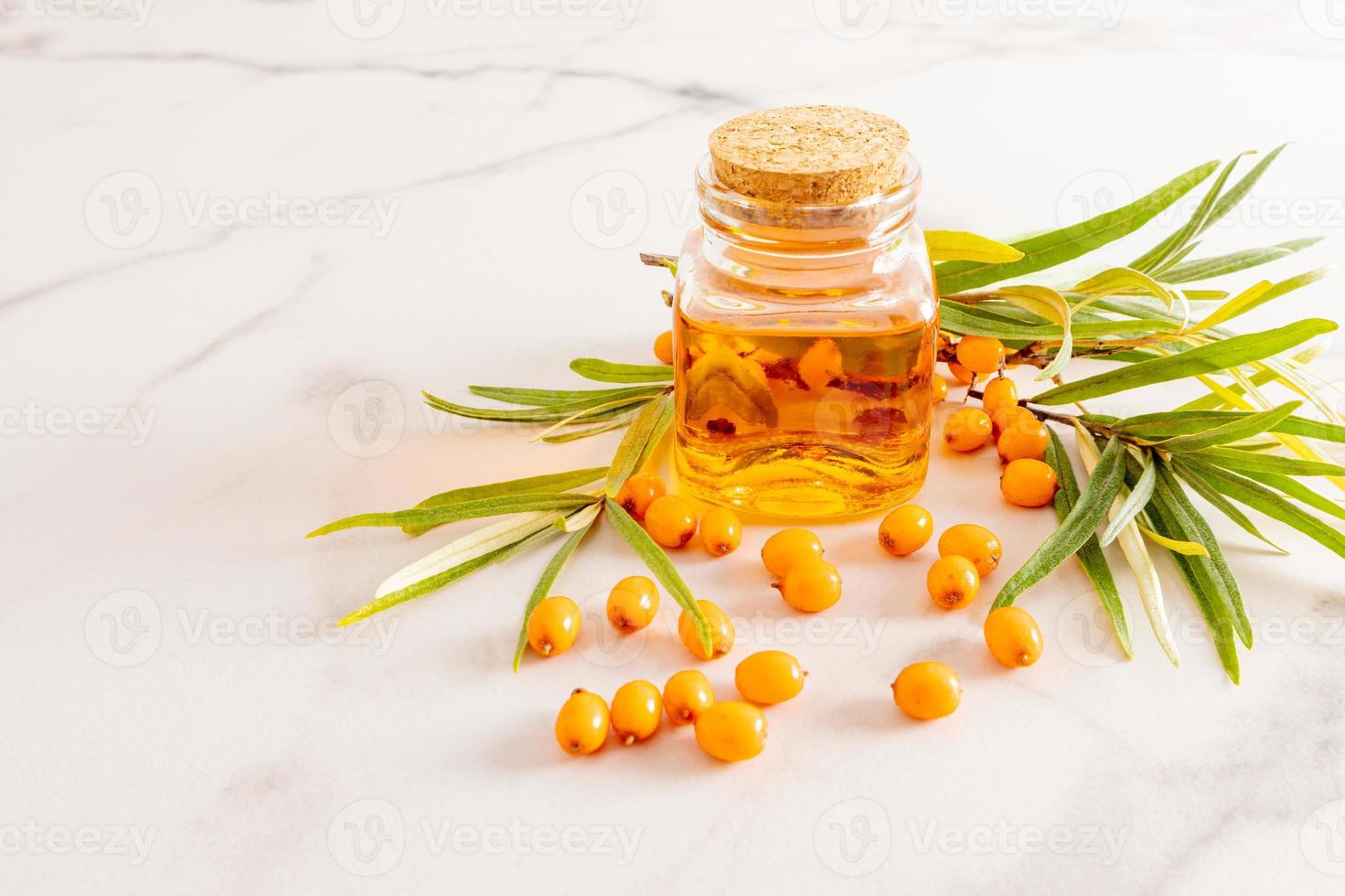 front view of a glass jar with a lid and organic sea buckthorn oil against the background of a branch and berries. natural medicine. photo