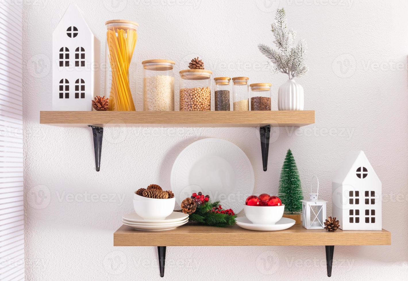 vista frontal de estantes de cocina abiertos con tarros ecológicos para productos a granel y adornos navideños. casitas de cartón blanco, conos naturales. foto