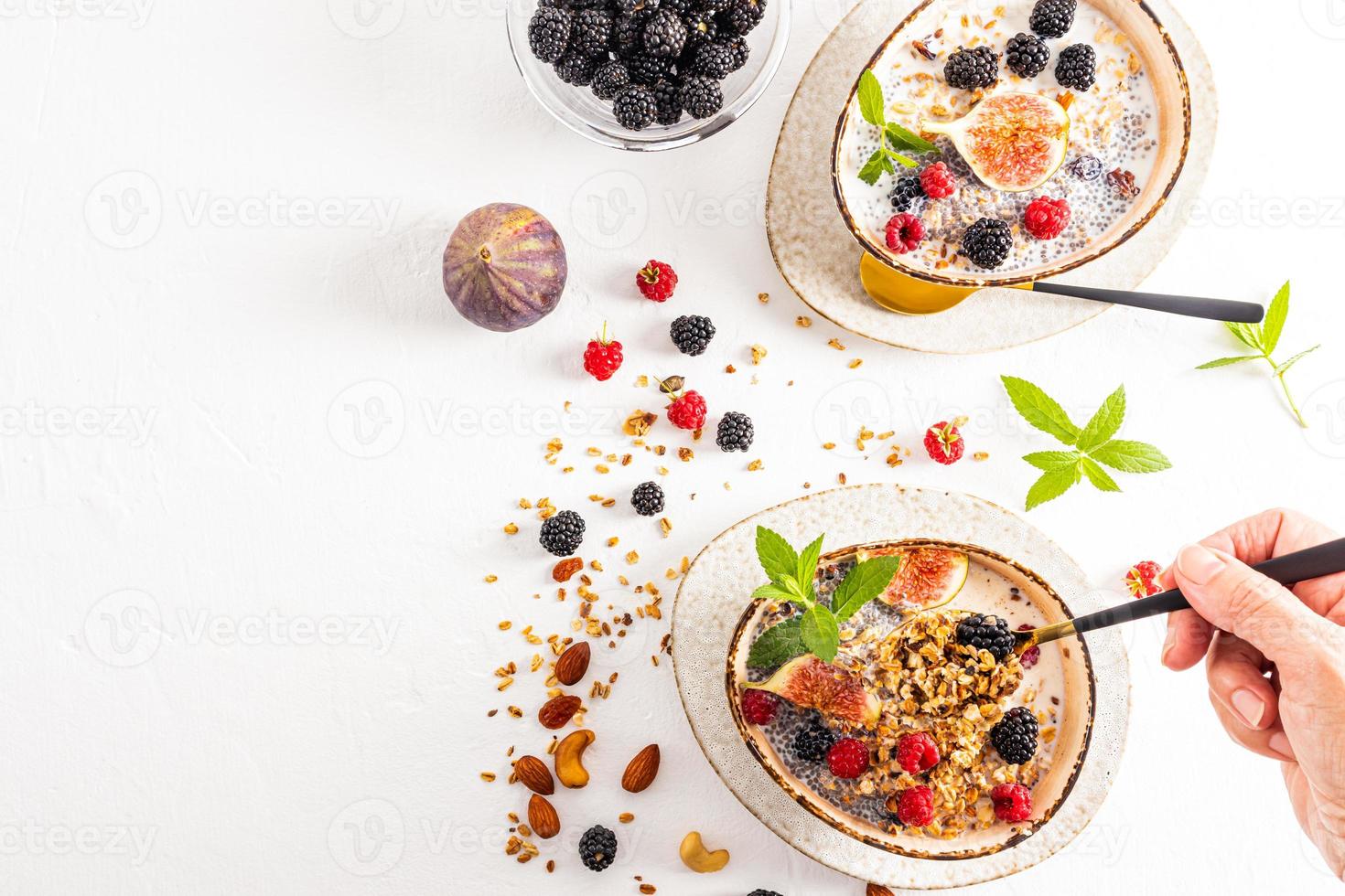 breakfast for two. cooked delicious granola in ceramic bowls with nuts, berries, mint and figs. a woman's hand holds a spoonful of muesli. photo