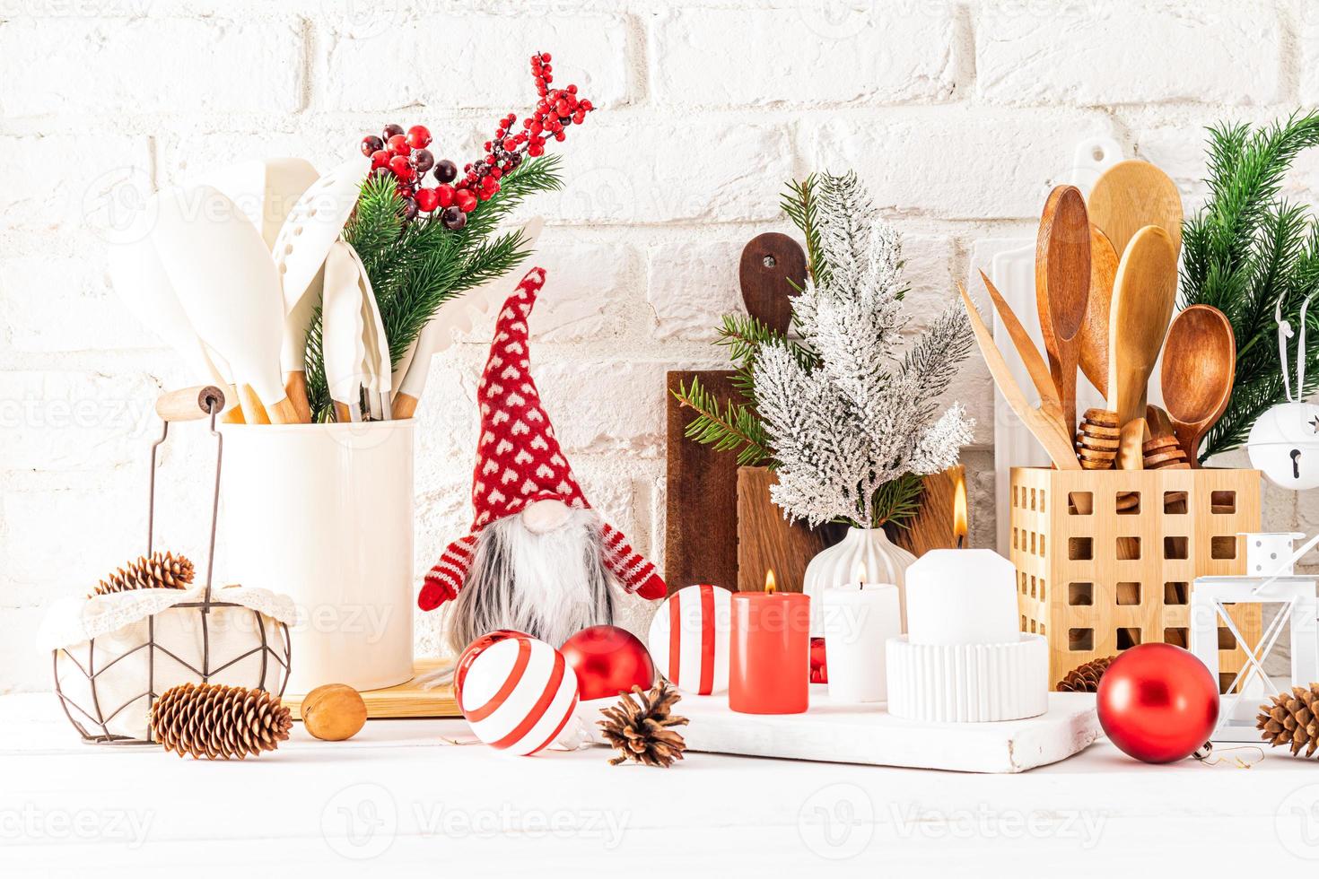 un fragmento de una encimera de madera blanca con varios utensilios de cocina y adornos navideños. velas, bolas, ramas de abeto. foto