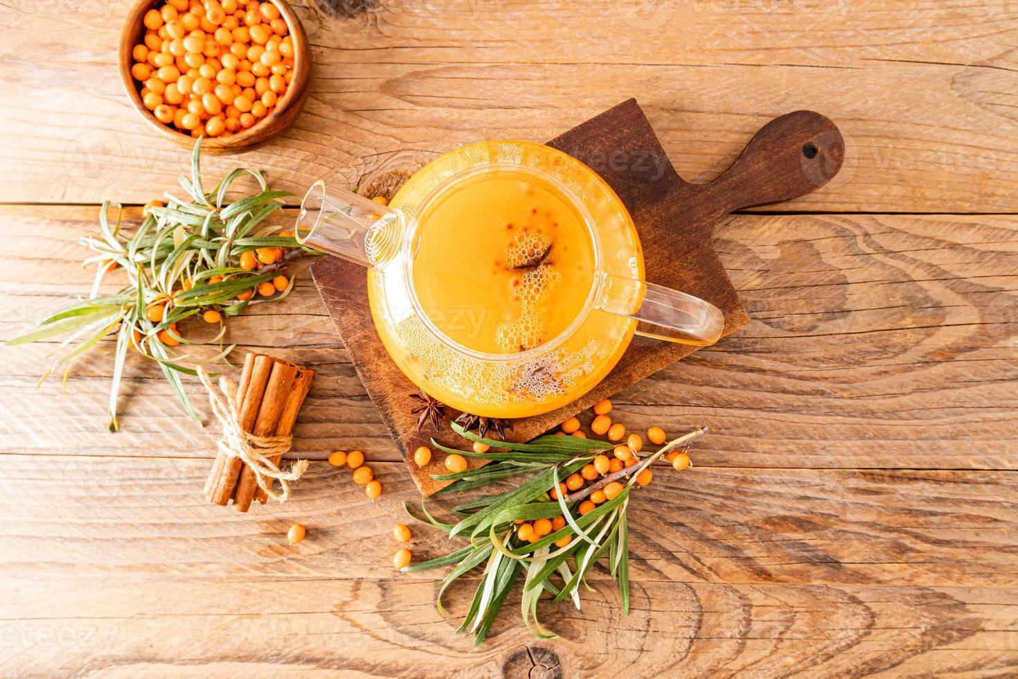 a glass teapot with hot sea buckthorn tea on a wooden board among the branches sea buckthorn. rustic style. improvement of the body. photo