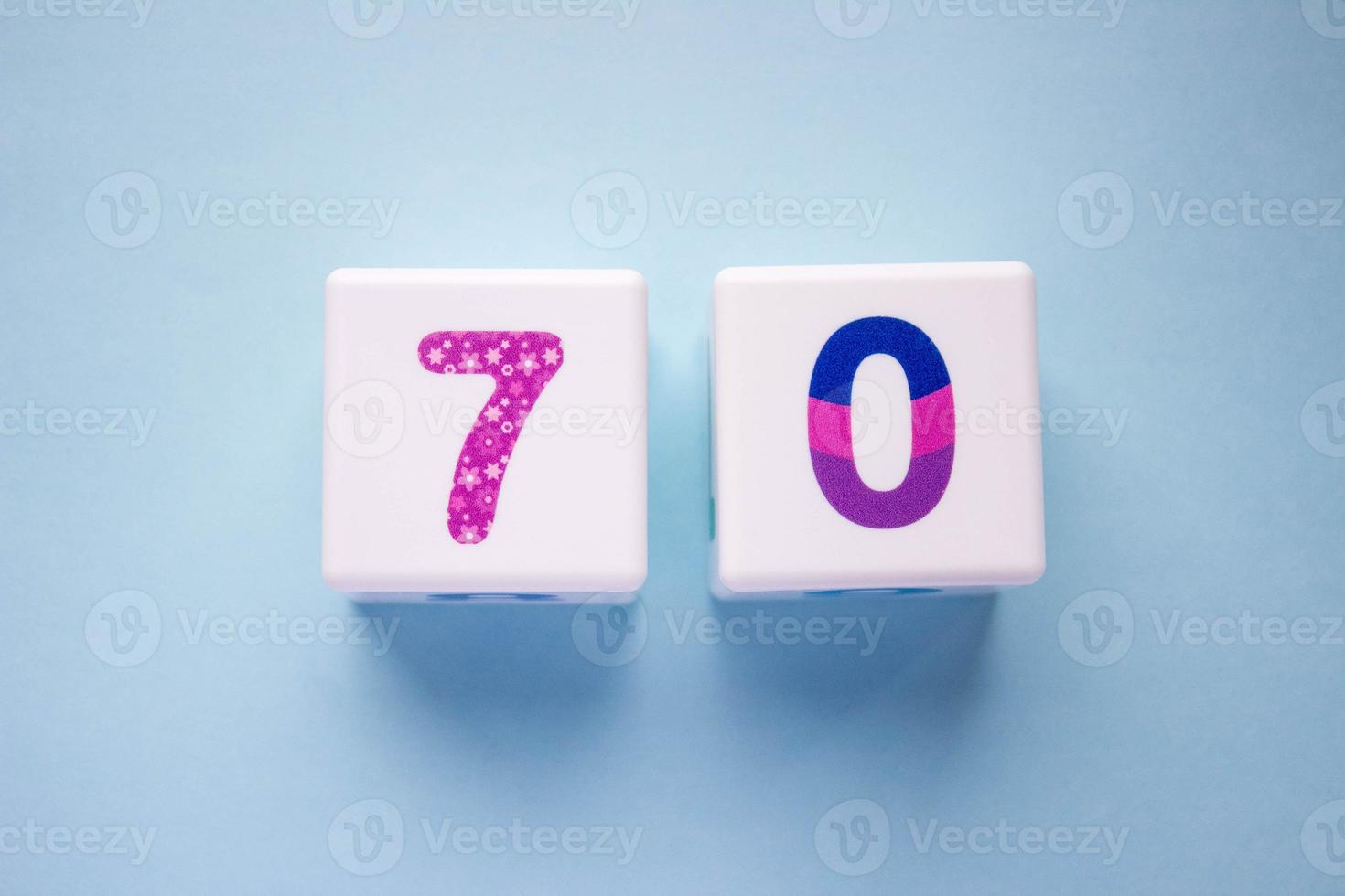 Close-up photo of a white plastic cubes with a colorful number 70 on a blue background. Object in the center of the photo