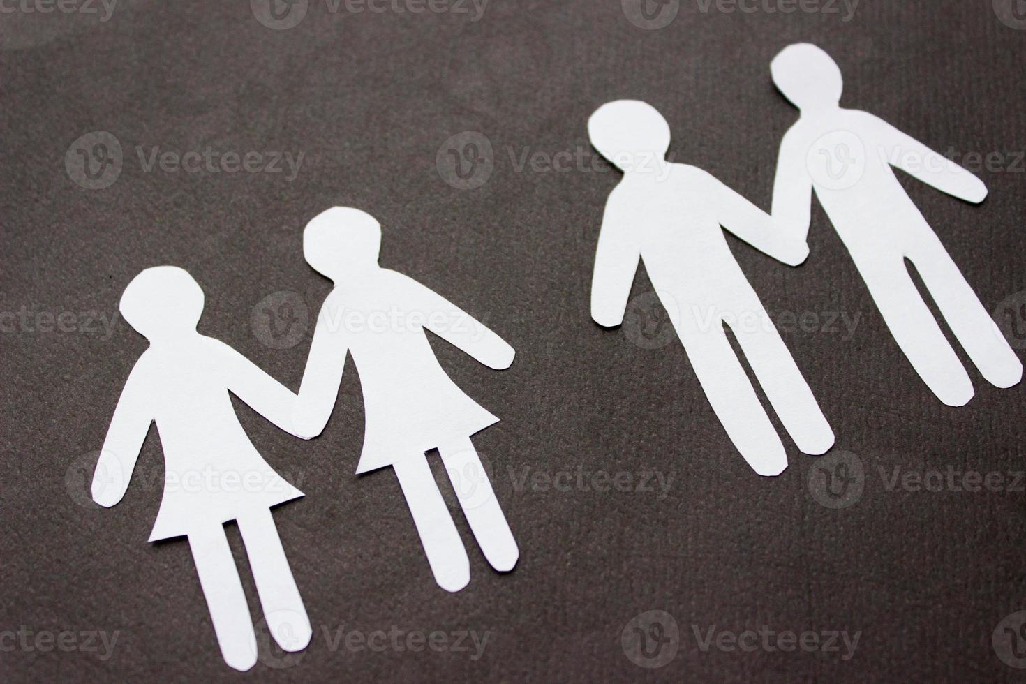 Two same-sex couples of people holding hands cutting from white paper on black background. A couple of women and a couple of men. Concept of same sex love, relationship, gender identity photo