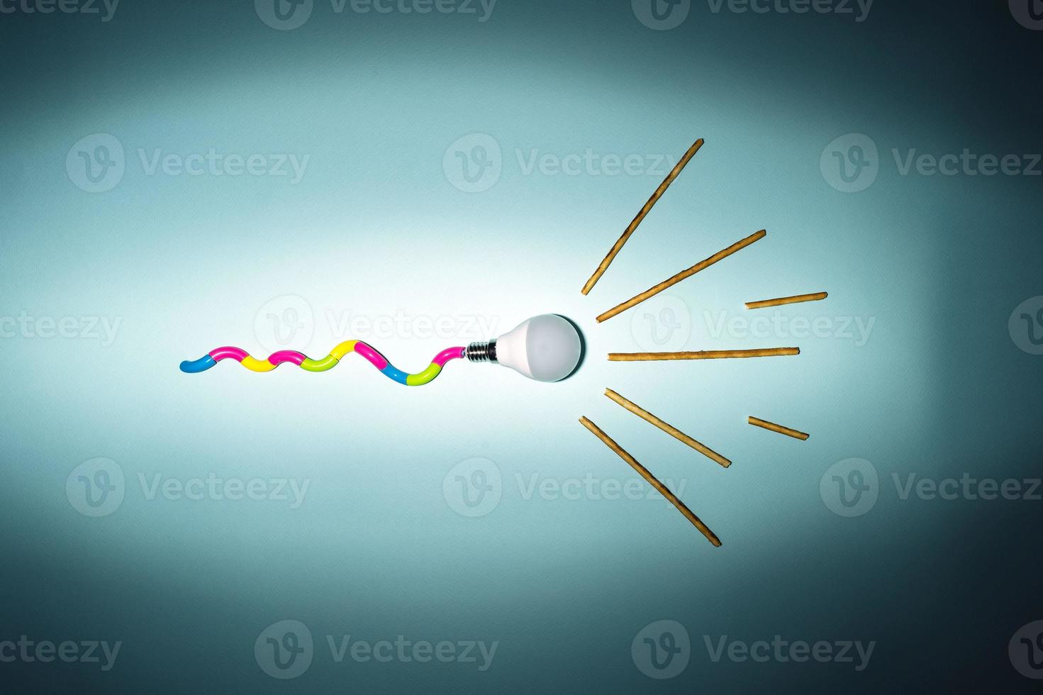 A creative composition of a light bulb and rays of light, a minimalistic concept, a tadpole, on a turquoise background photo