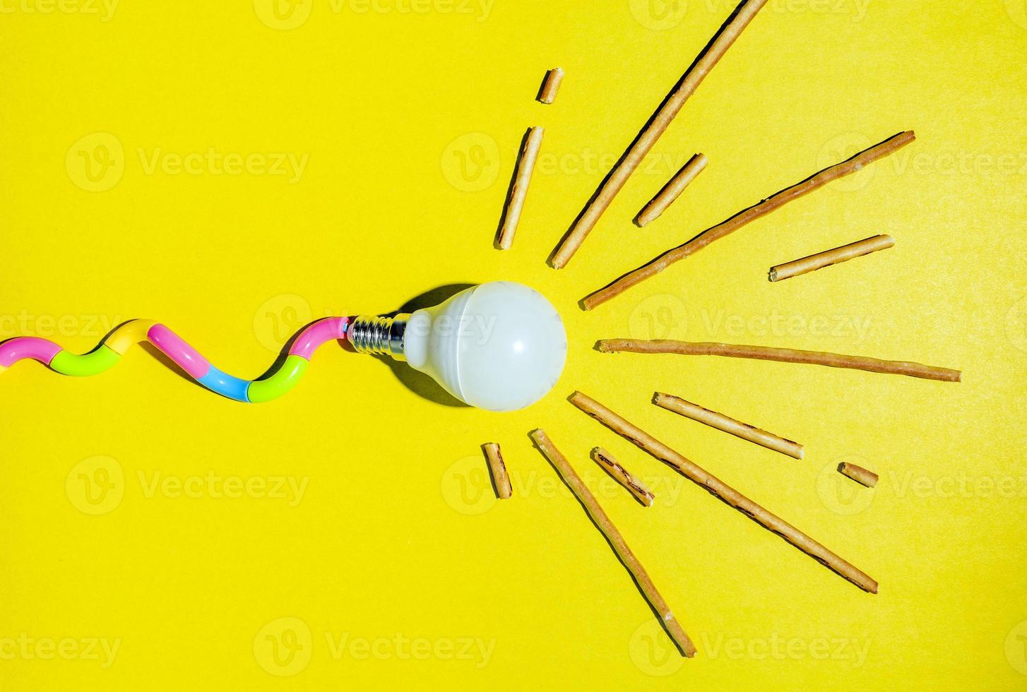 A creative composition of a light bulb and rays of light, a minimalistic concept, a tadpole, on a yellow background. photo