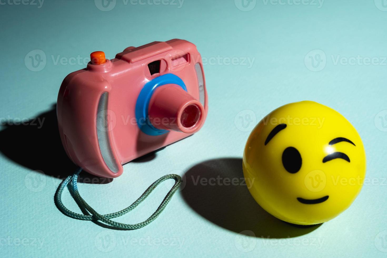 A children's toy camera and a smiley face on a turquoise background, the concept of minimalism. A creative composition photo