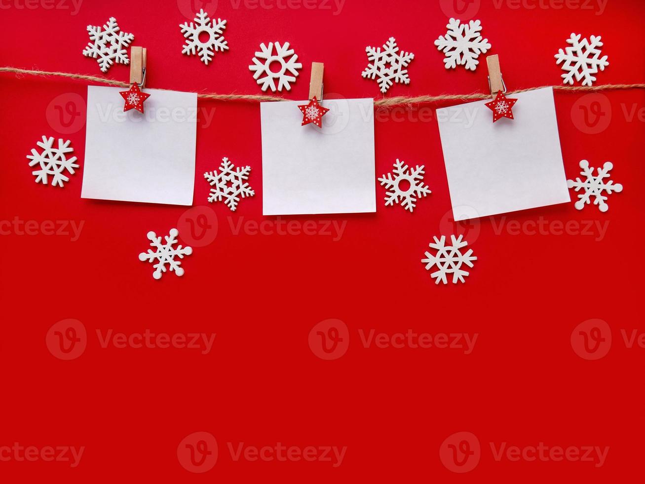 Christmas red background with white snowflakes. Three sheets of paper with space for text on a rope. Topview, copy space photo