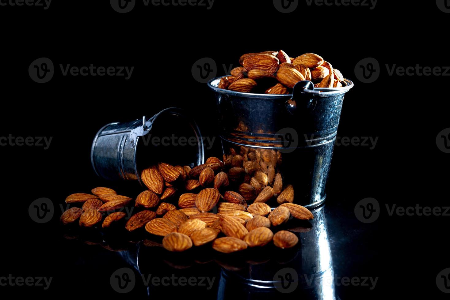 Peeled almond in jar wineglass bucket on a black isolated background. Row of bowls with almond nuts, front view. photo