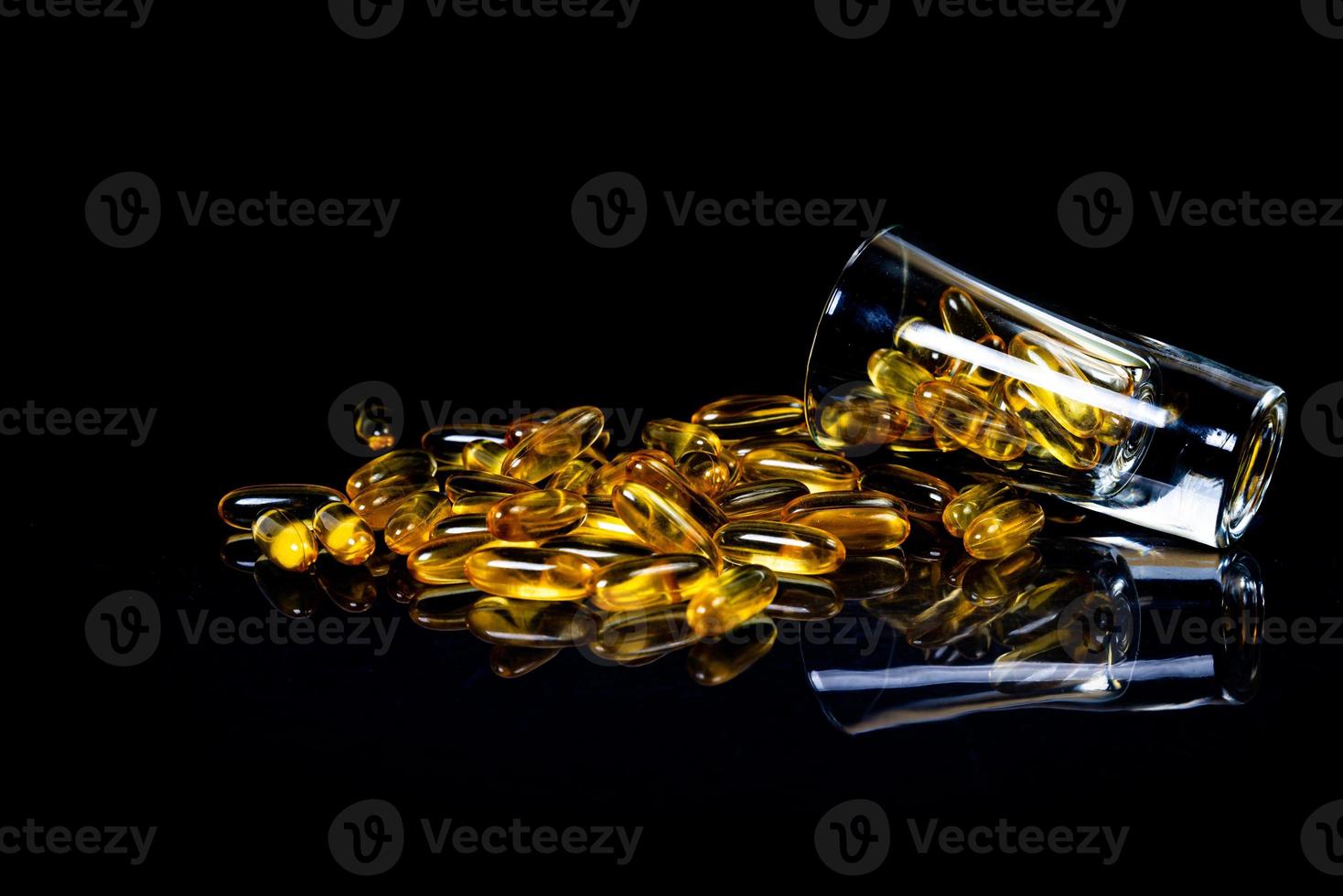 cápsulas de aceite de pescado. Píldoras amarillas de omega 3 en frasco en negro oscuro. cápsulas de aceite de pescado en copa de vino. en tarro en ampollas cubo foto