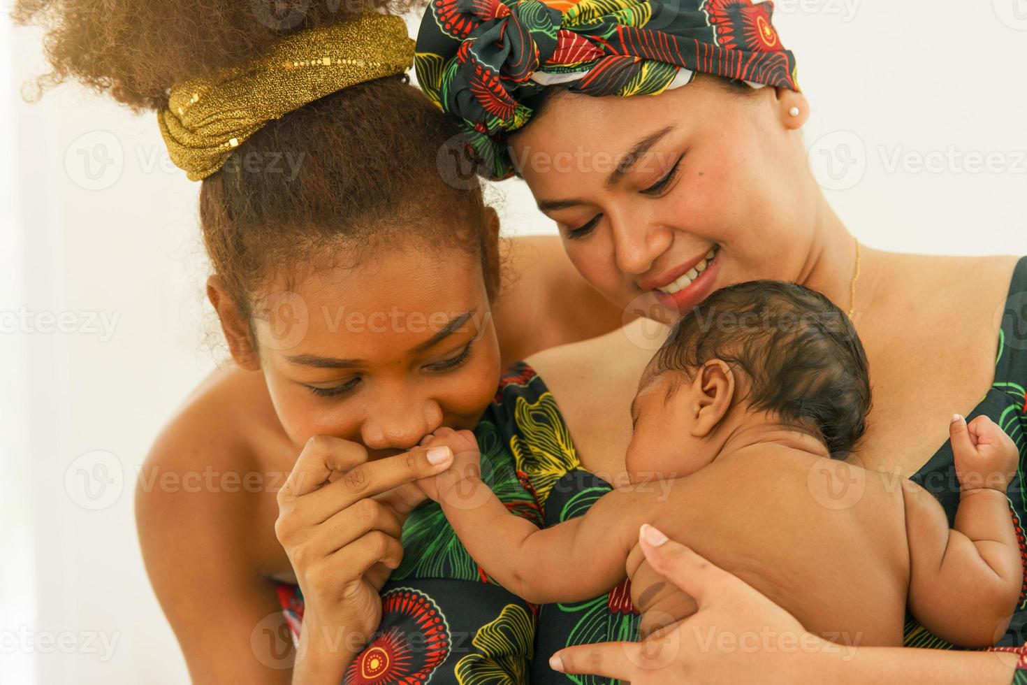 Mother and eldest daughter in traditional dress native-style African carry newborn baby one-month-old breastfeeding. Happy infant mixed race afro-Asia sleep well in warm embrace of motherhood. photo