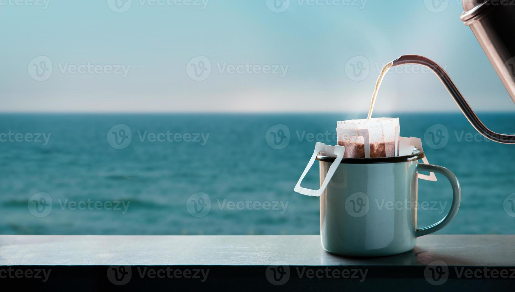 Dripping Coffee by the Sea Side at Morning. Making Hot Drink by Pouring Hot Water from kettle into an Instant Coffee Drip Bag at the Balcony. Relaxing with Harmony Living Lifestyle photo