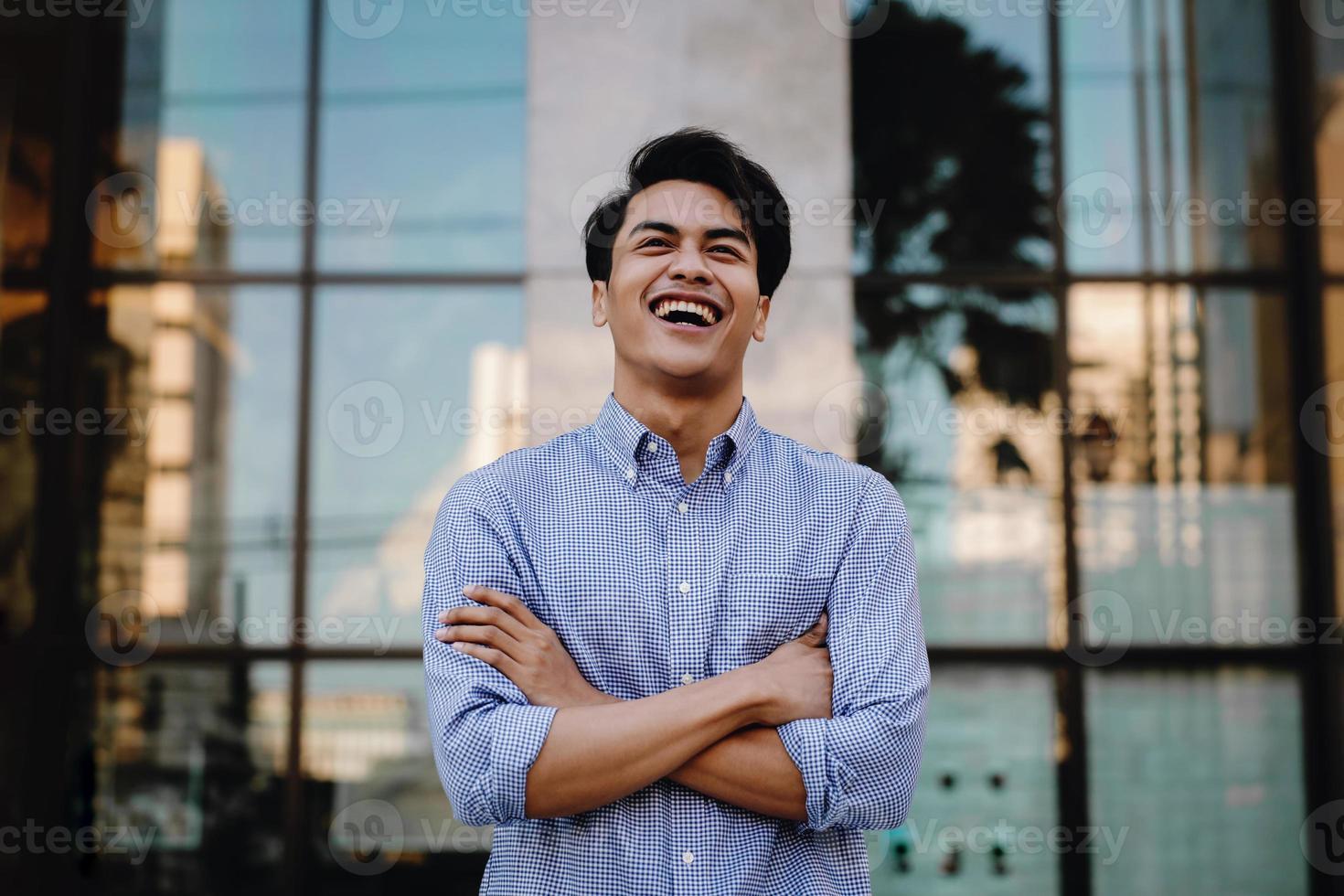 Portrait of Laughing Young Asian Businessman in the City. Crossed Arms and looking away. a Happy Friendly Man photo