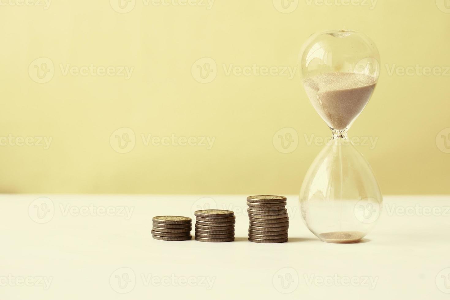 hourglass and stack of coins on table, photo