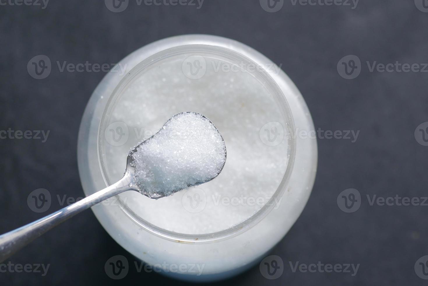 white sugar and spoon in a container on black background, photo