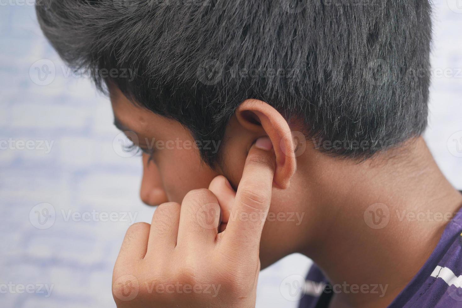 teenage boy having ear pain touching his painful ear , photo