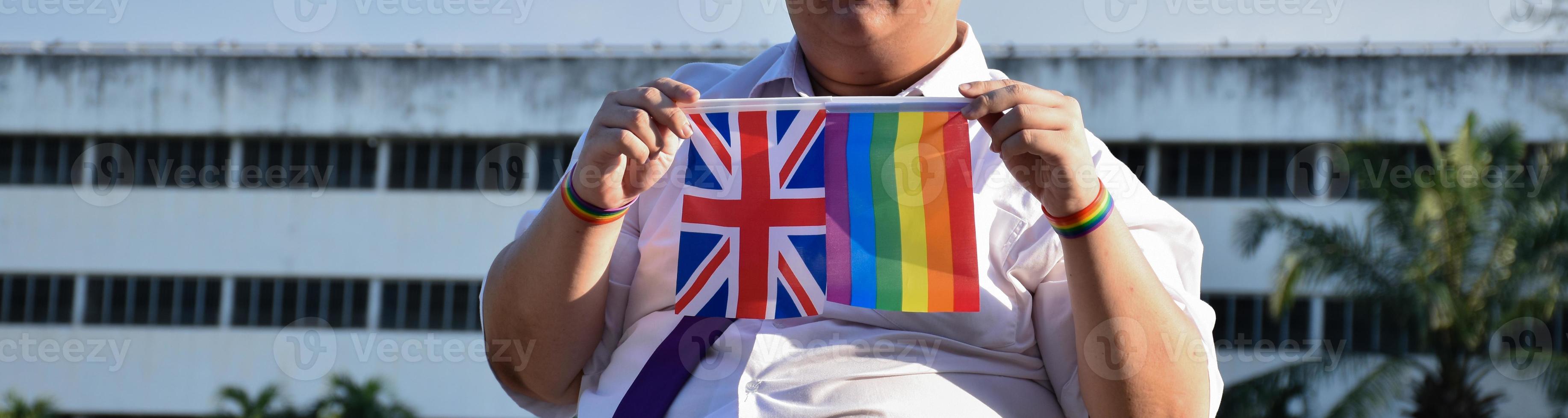 Union Jack flag and rainbow flag raising in hands and against bluesky, soft and selective focus, concept for LGBT celebrations and LGBT events in pride month in UK. photo