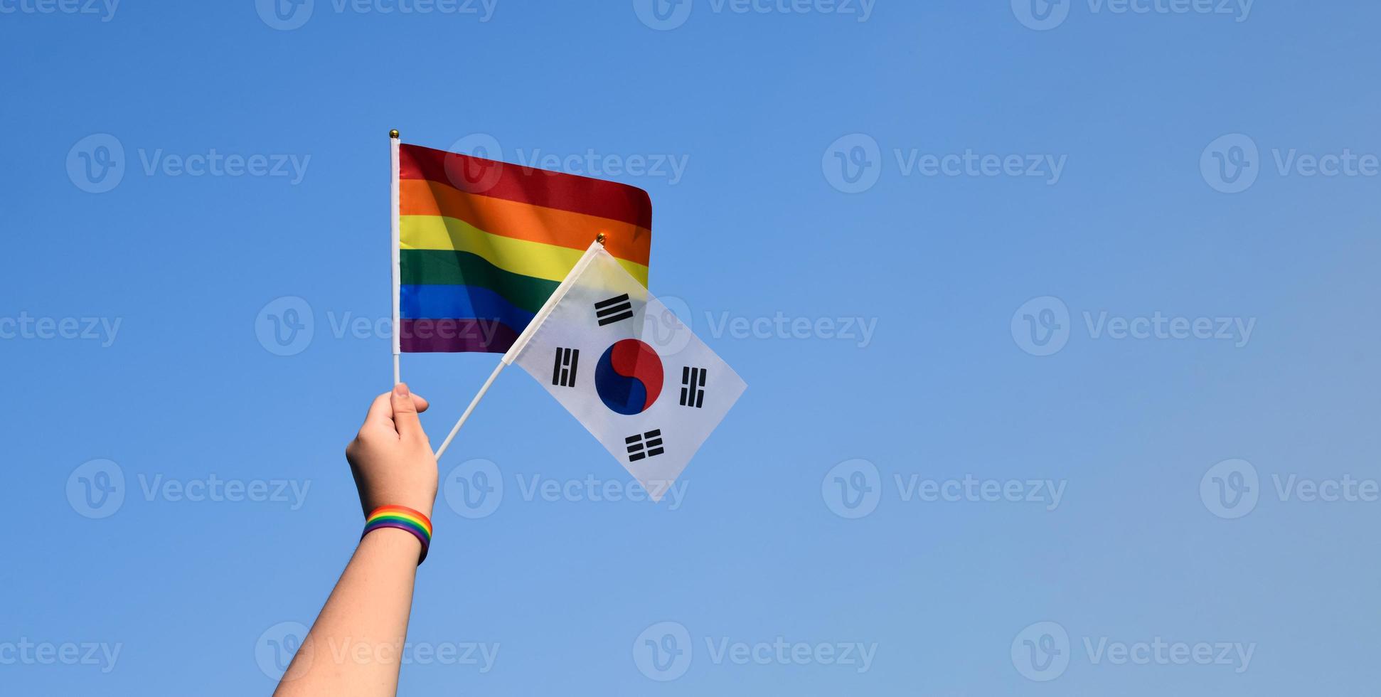 South Korea flag and rainbow flag raising in hands and against bluesky, soft and selective focus, concept for LGBT celebrations and LGBT events in pride month in South Korea. photo