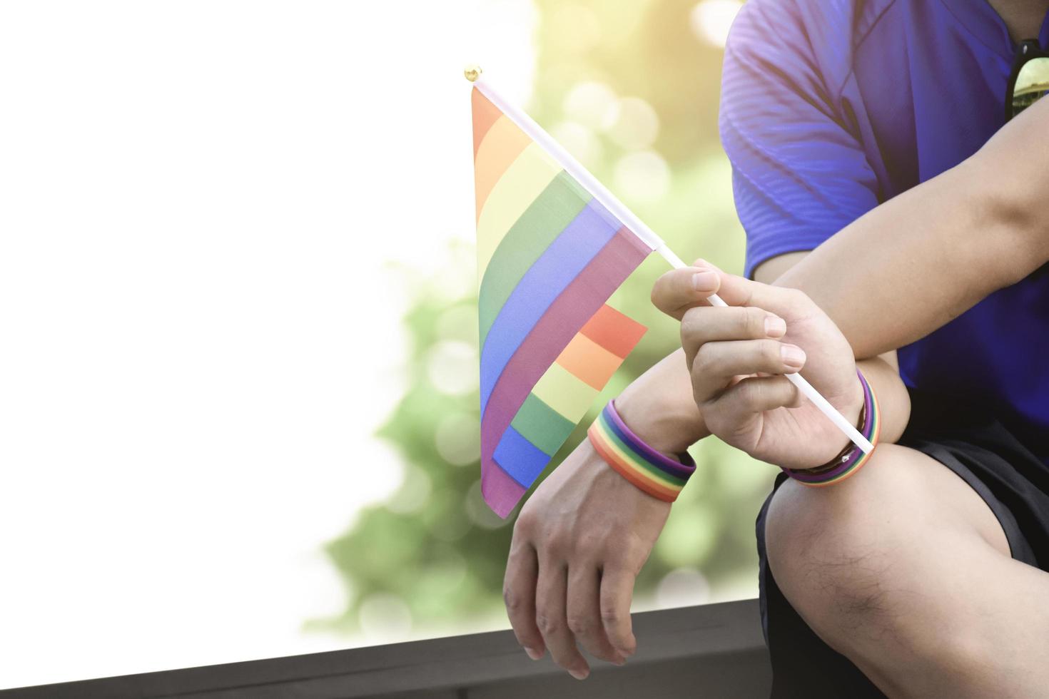 Rainbow flag holing in hand of asian gay which wears rainbow wristband to call out and shows LGBT gender diversity and respecting gender alternative around the world. photo