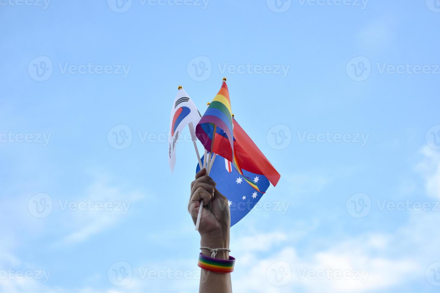 Rainbow flags and flags of many countries holding in hand against bluesky, concept for celebration of lgbtqai genders in pride month around the world, soft and selective focus. photo