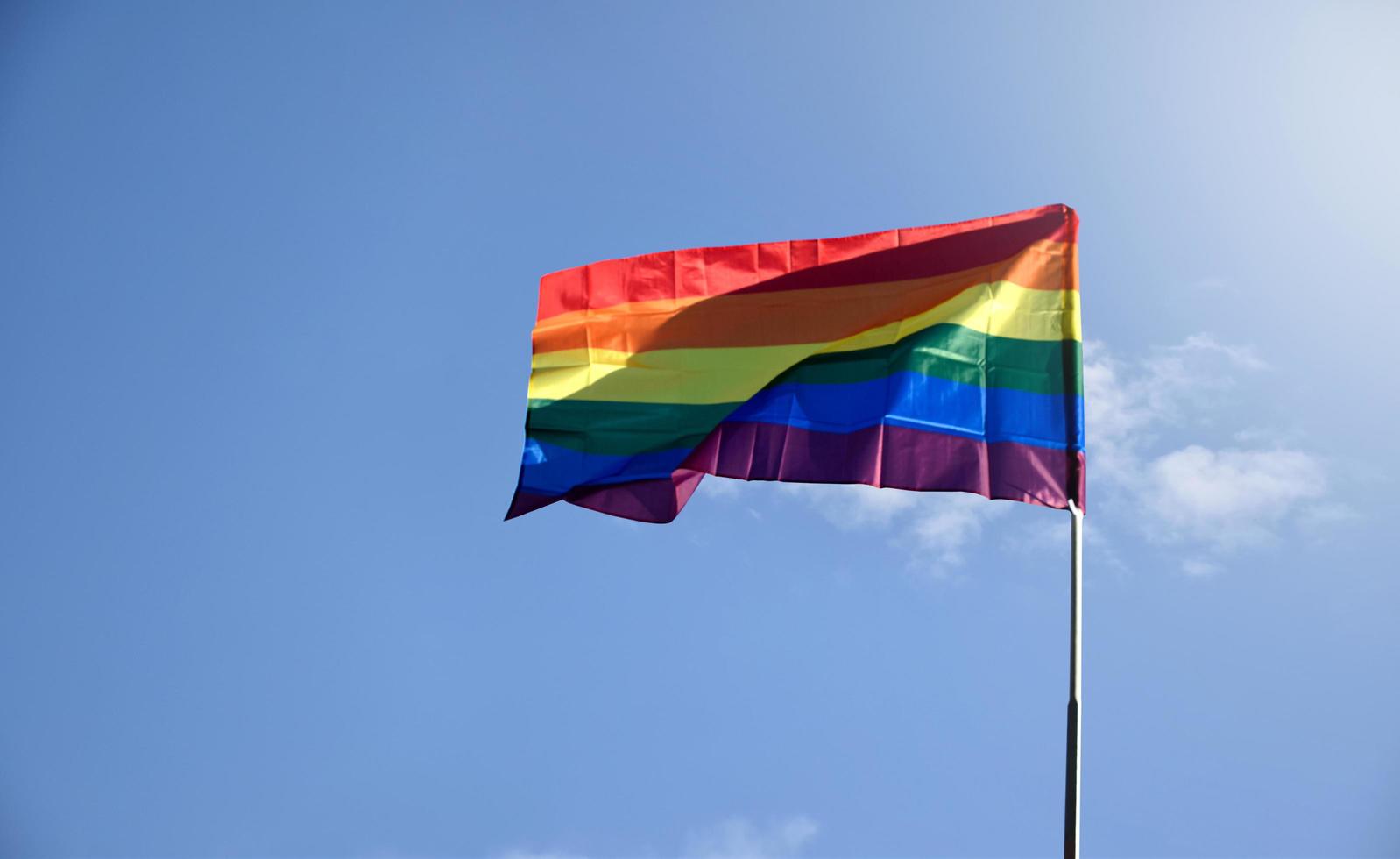 LGBT rainbow flag waving and holding in hands against blue sky in afternoon of the day, soft and selective focus, concept for lgbtqai celebration in pride month around the world. photo