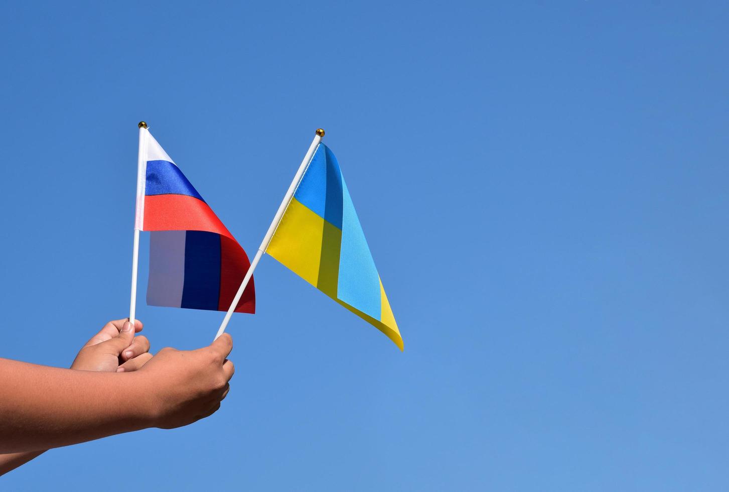 bandera nacional rusa y bandera nacional ucraniana cogidas de la mano contra el fondo azul, enfoque suave y selectivo. foto