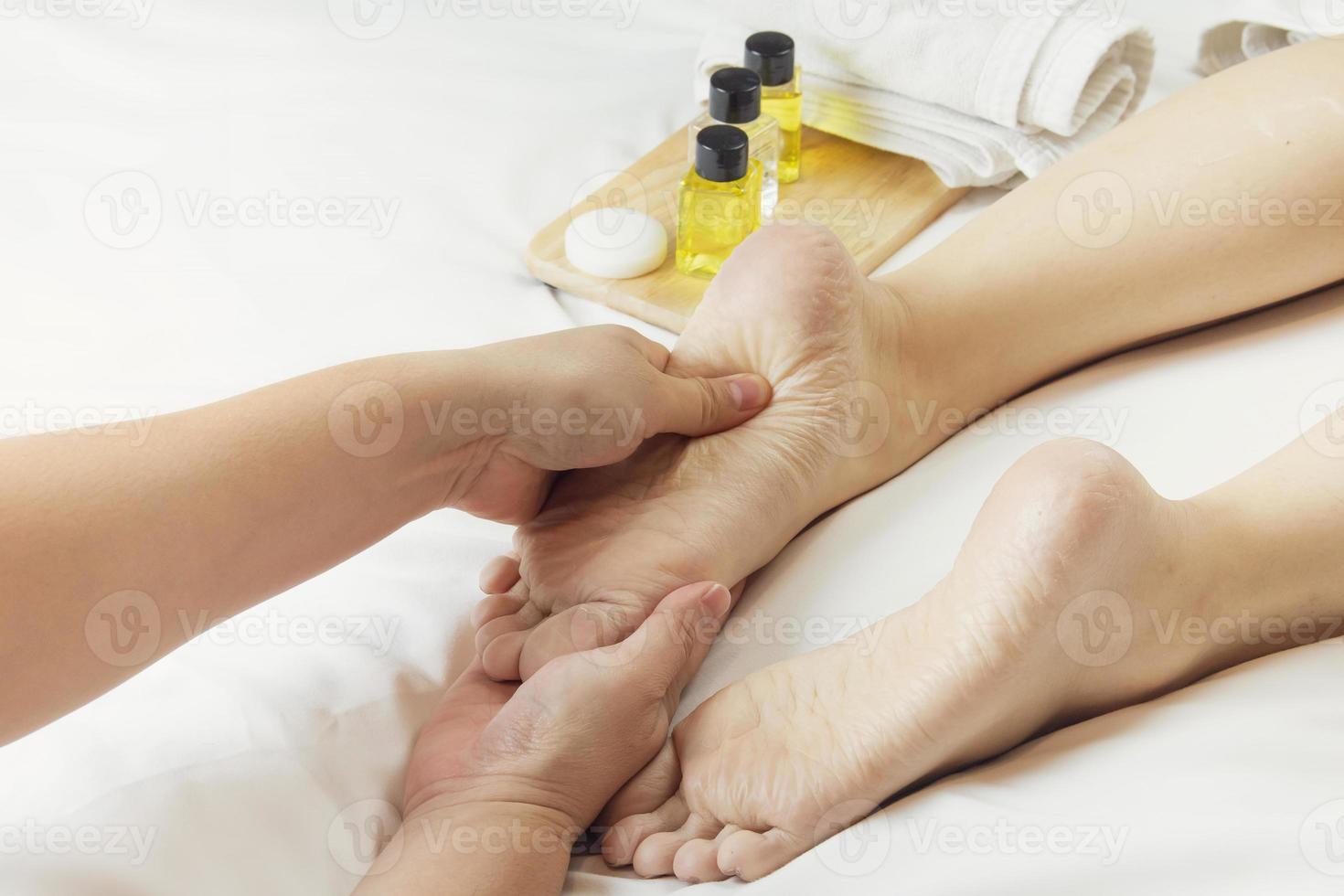 Hands of a professional foot massager with oils and health care products on white bed. Concept of health care, relaxation, foot spa treatment. or product introduction for women's foot spa photo