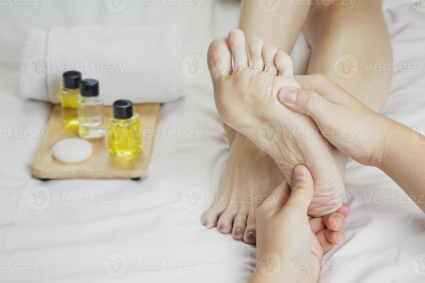 Hands of a professional foot massager with oils and health care products on white bed. Concept of health care, relaxation, foot spa treatment. or product introduction for women's foot spa photo