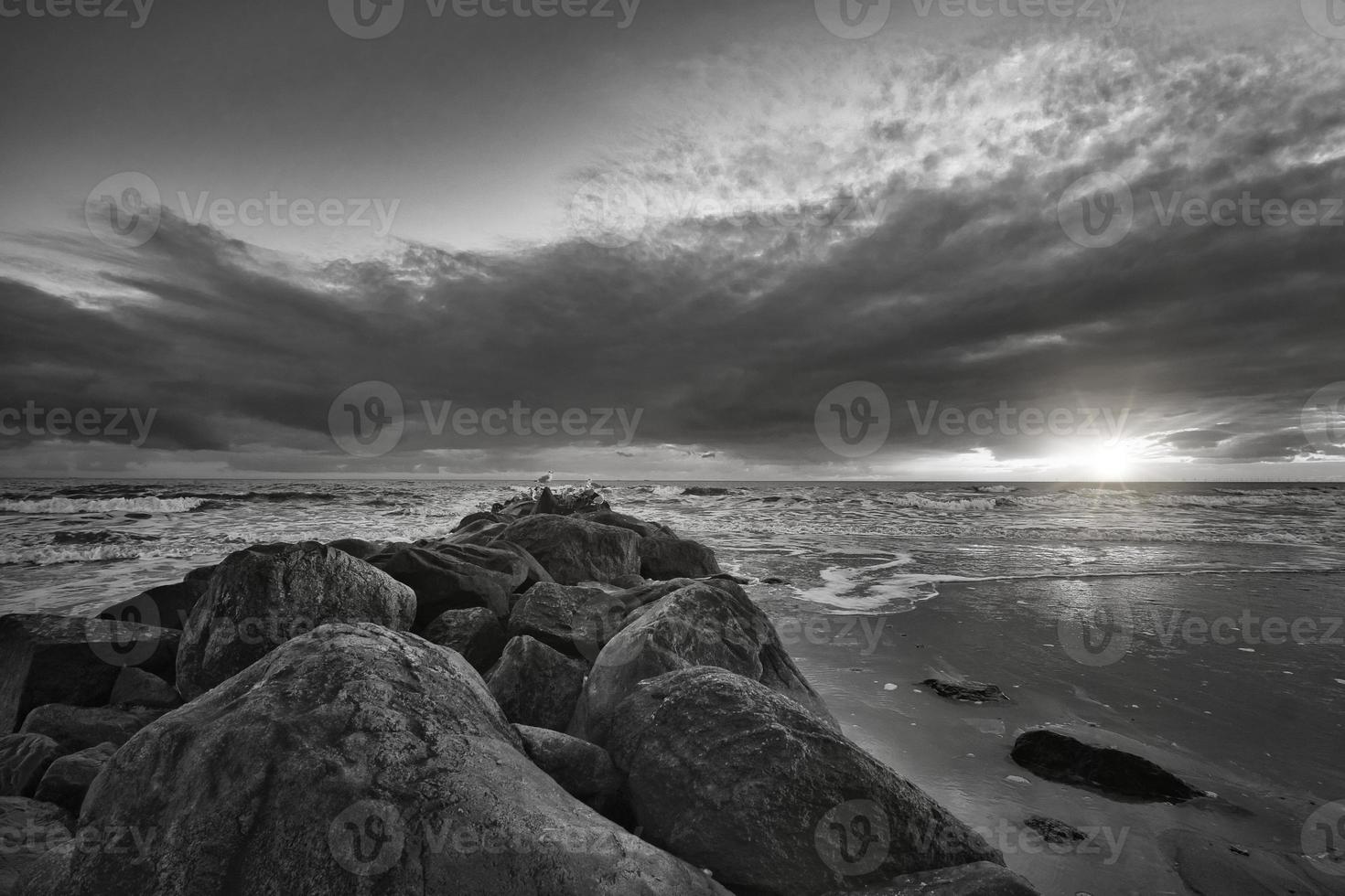 puesta de sol en la playa en dinamarca tomada en blanco y negro. espigón de piedra foto