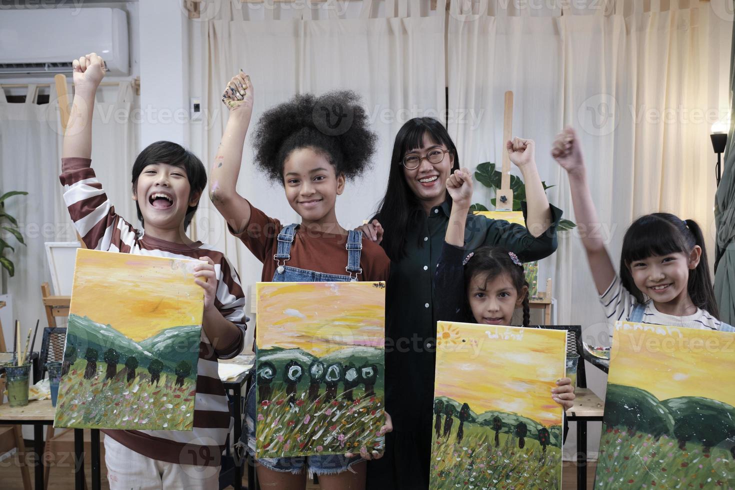 Group of art people in classroom studio, a teacher and student kids proud show painting work, an acrylic color picture on canvas, creative learning with talents skill at elementary school education. photo
