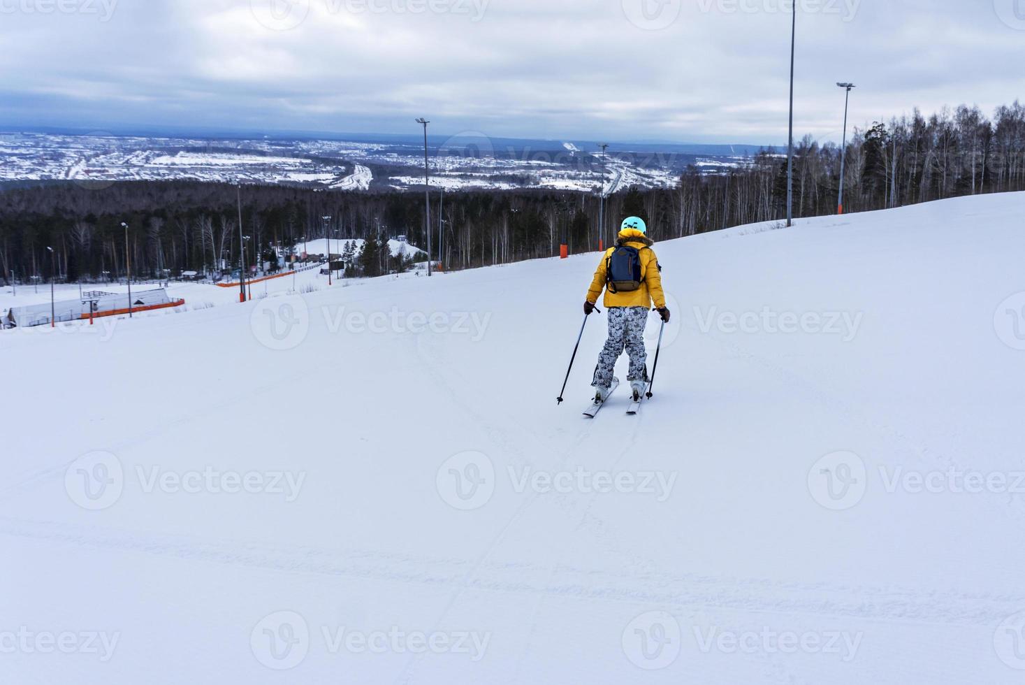 Young woman in yellow jacket and ski helmet skiing down on mountain slope, winter sports, alpine skiing outdoors activity, healthy lifestyle photo