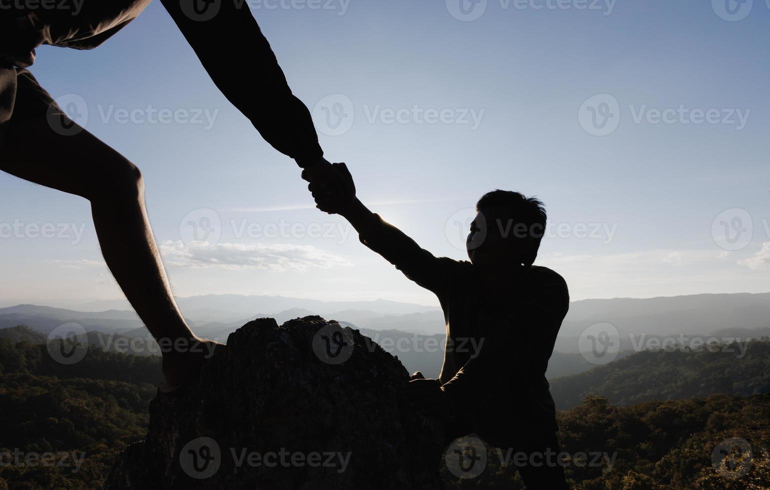 Silhouette of hiker helping each other hike up a mountain at sunset. People helping and, team work concept. photo