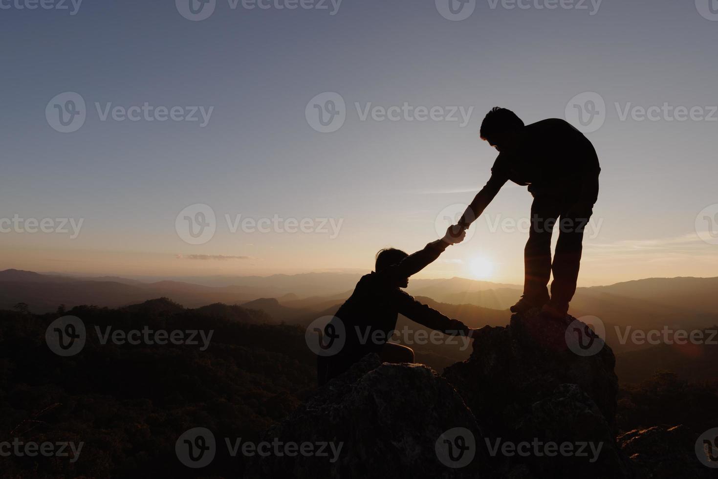 siluetas de dos personas subiendo a la montaña y ayudando. concepto de ayuda y asistencia. foto