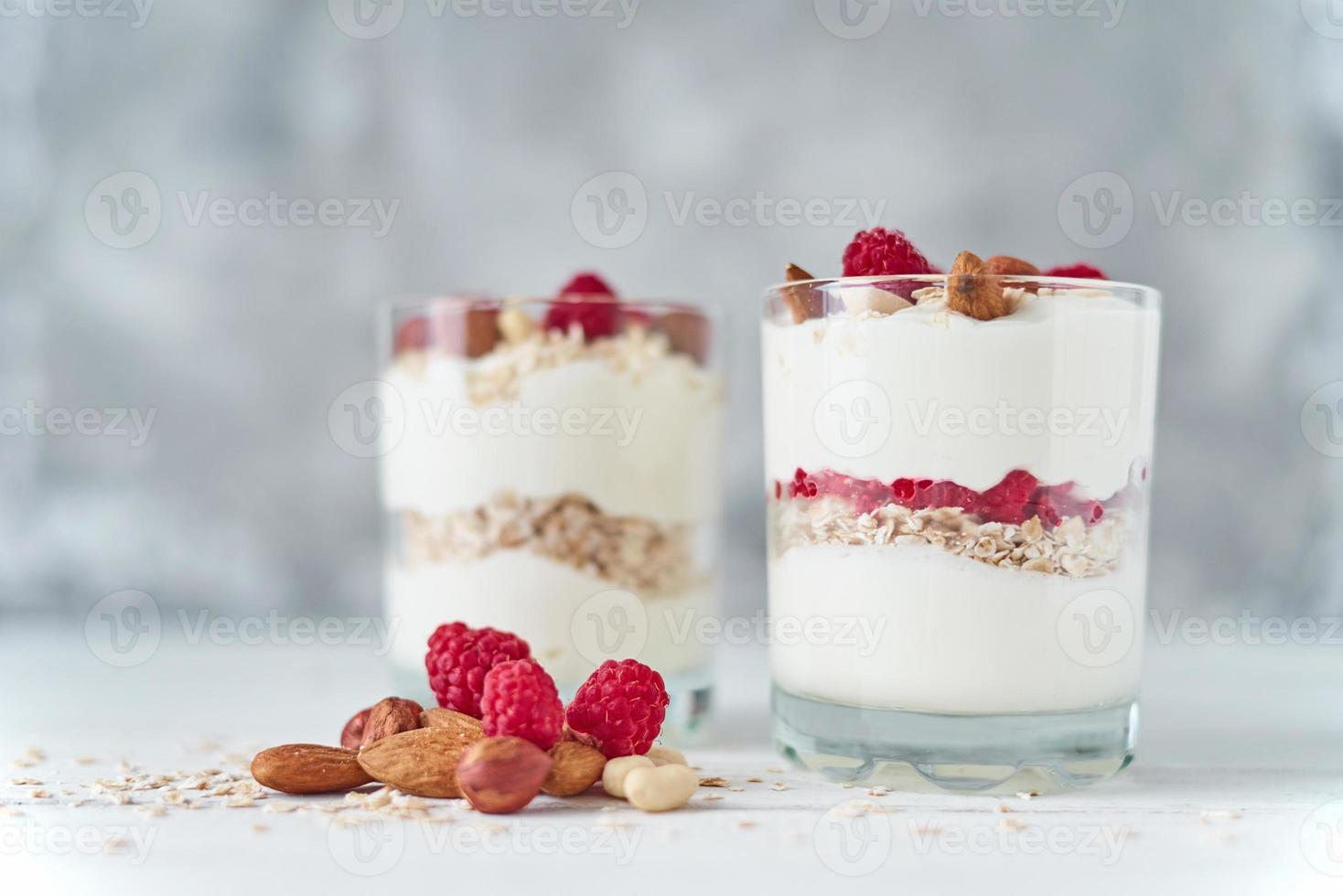 Two glasses of greek yogurt granola with raspberries, oatmeal flakes and nuts photo