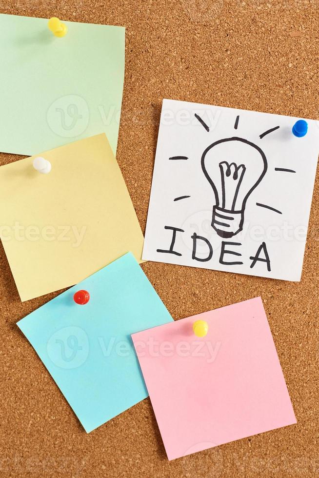 painted light bulb with word idea and colored blank notes on a cork board photo