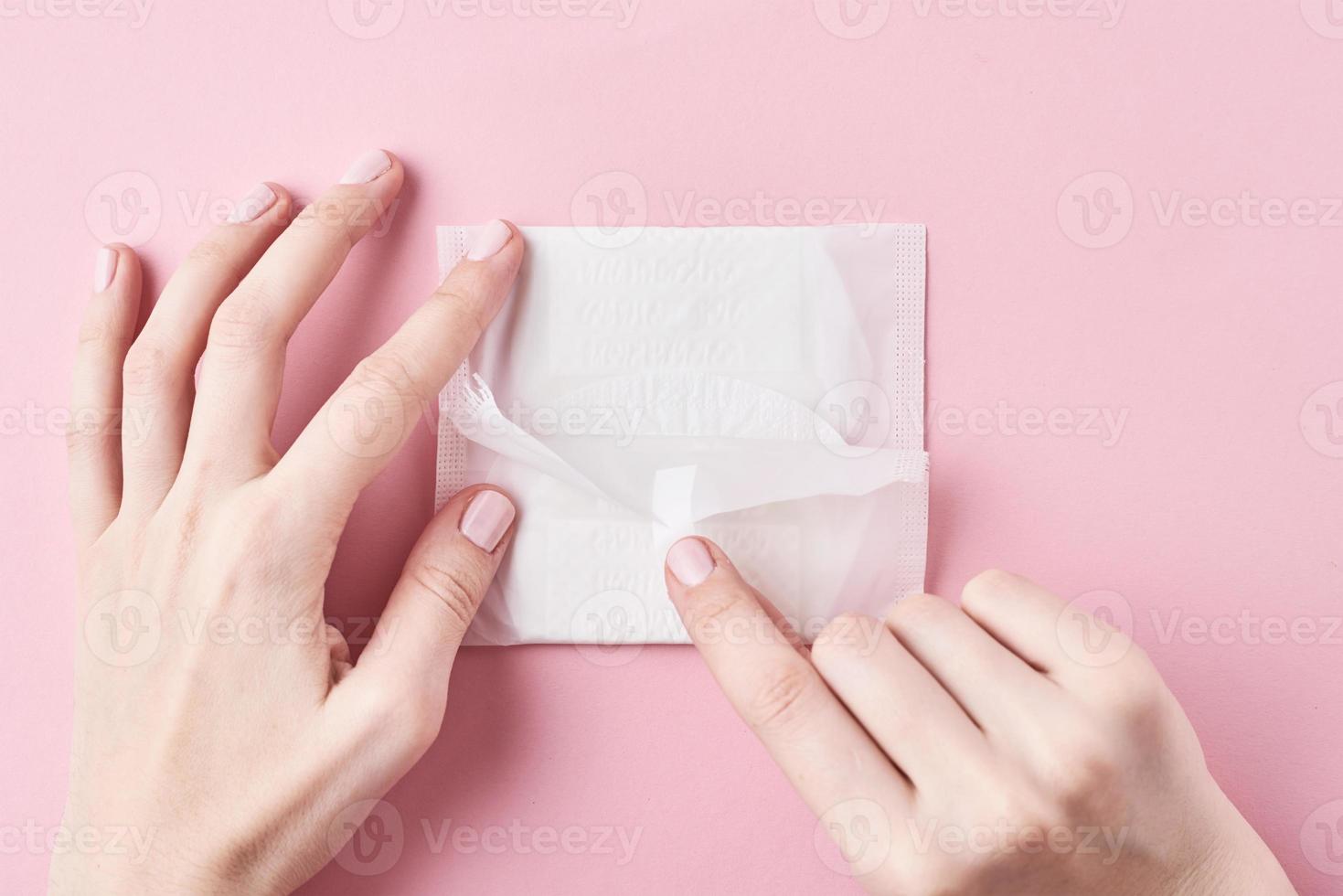 Woman hands hold sanitary pad on a pink background photo