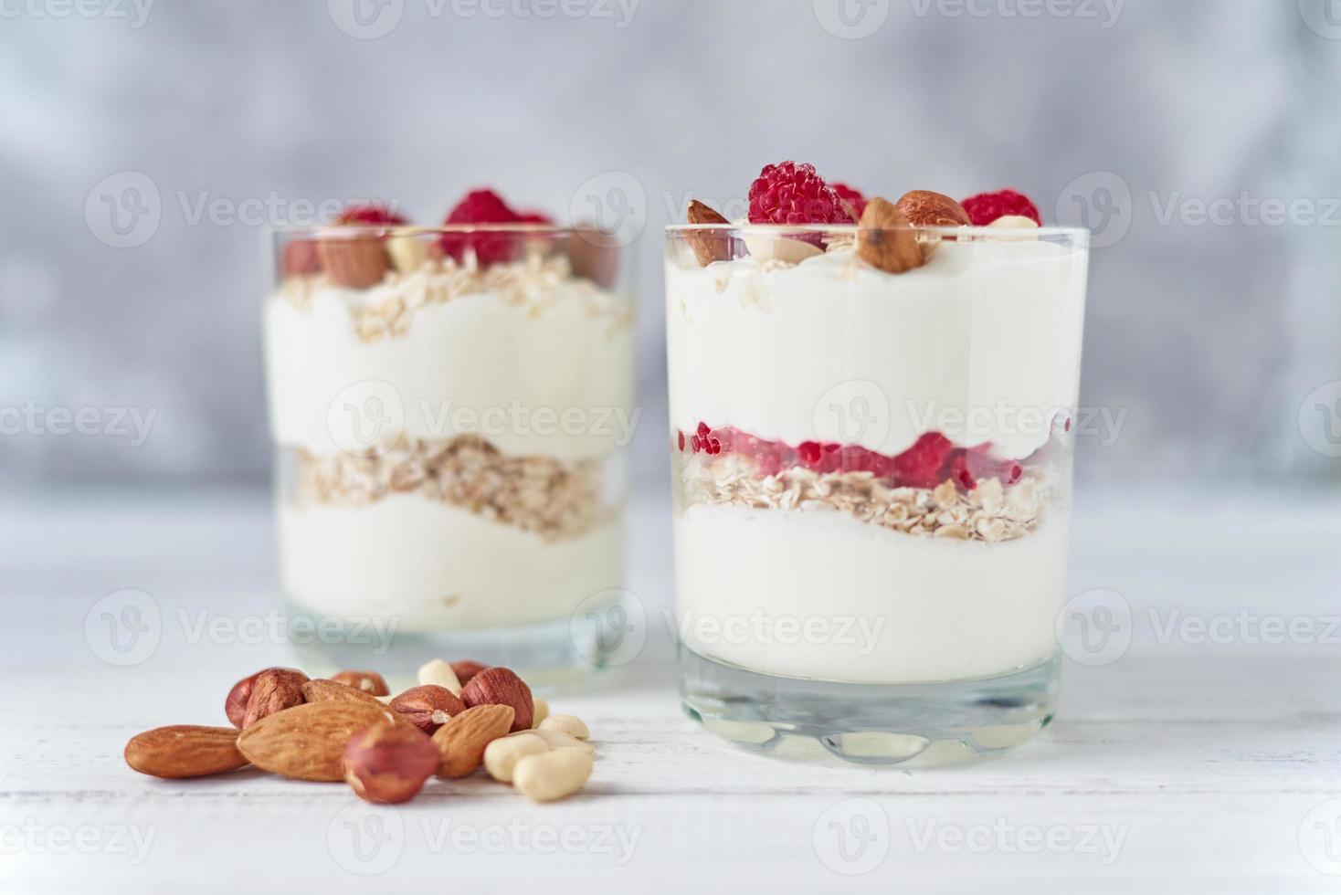Two glasses of greek yogurt granola with raspberries, oatmeal flakes and nuts photo