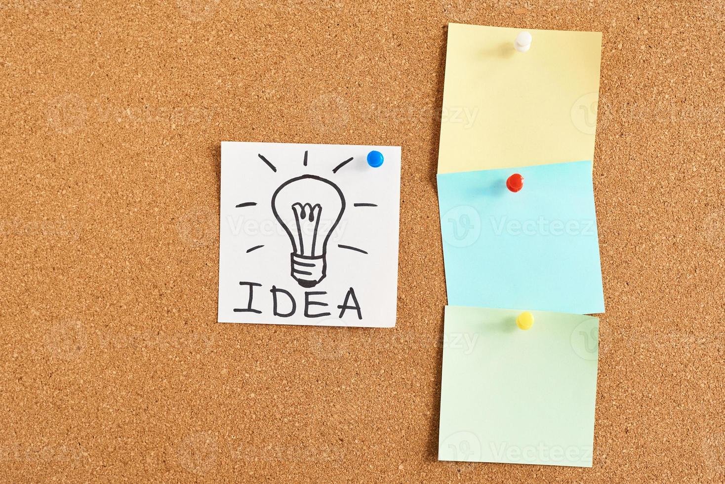 painted light bulb with word idea and colored blank notes on a cork board photo