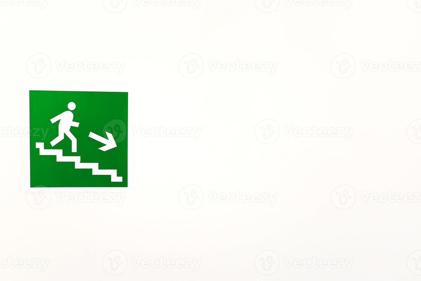 Green sign down the stairs on an empty bright wall photo