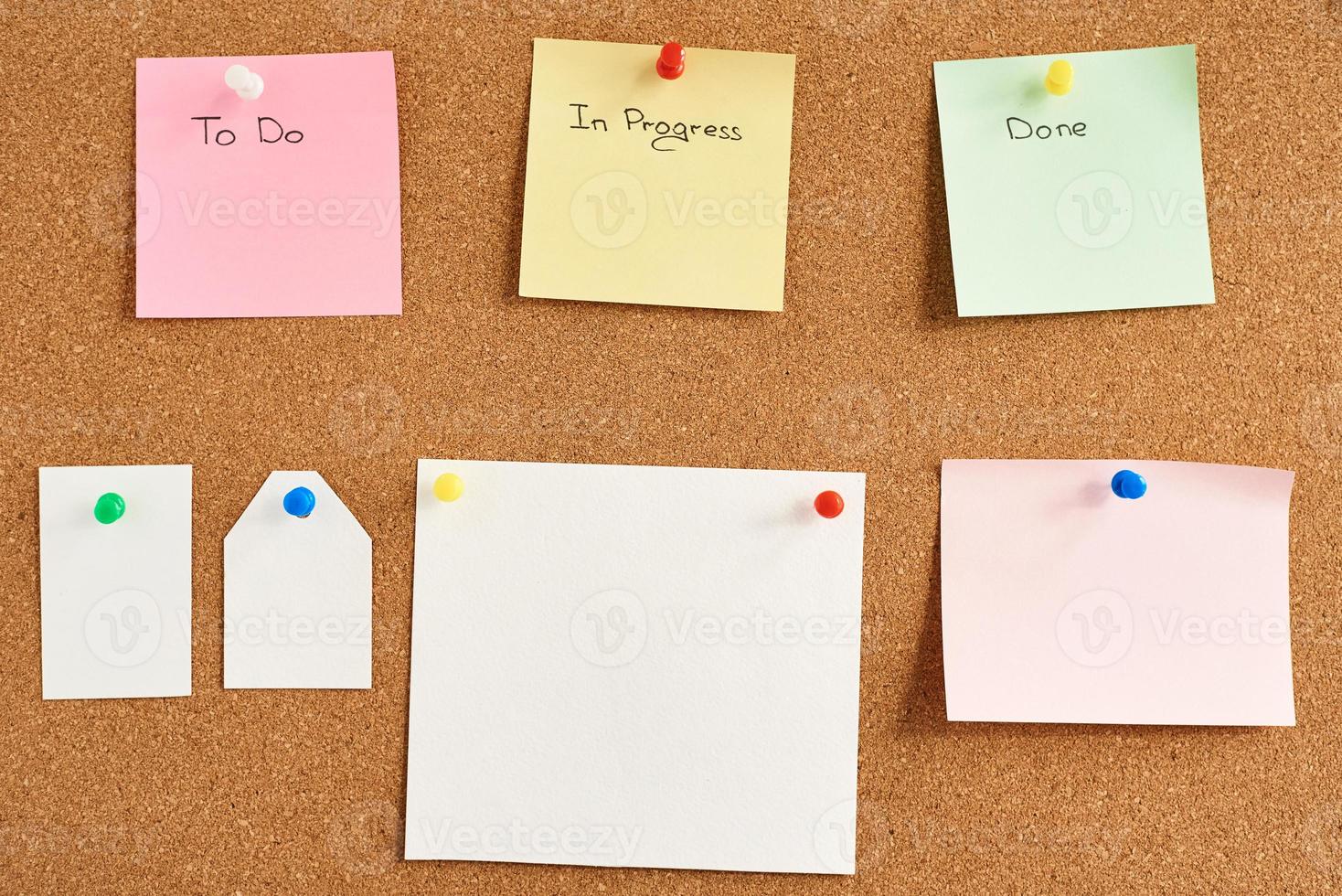Colorful paper notes with words To do, In progress and Done pinned on a cork board photo
