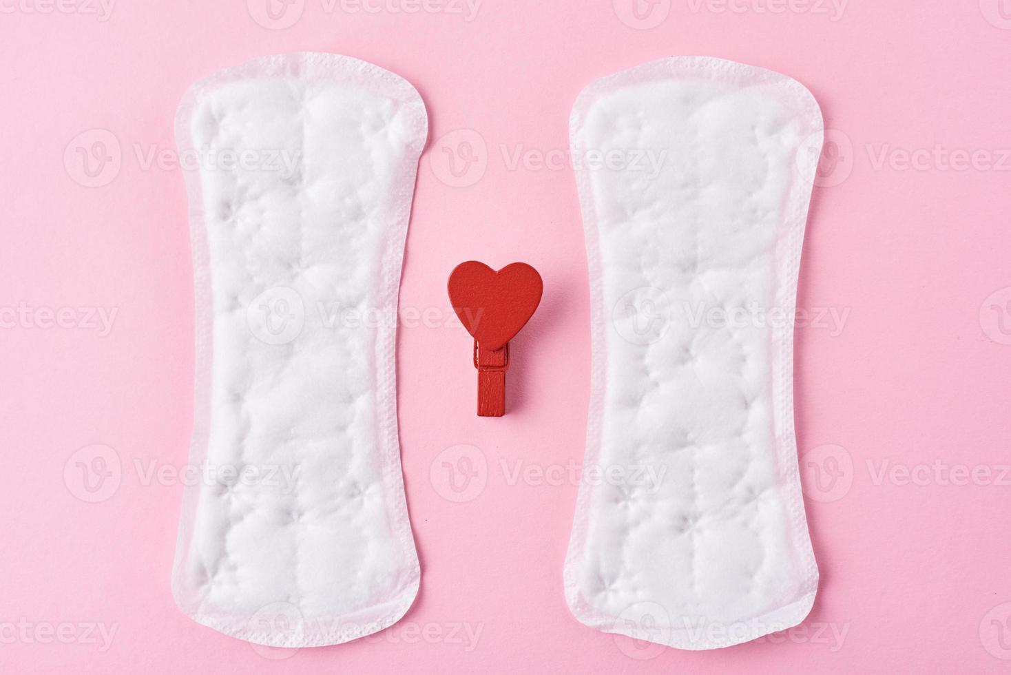 Two sanitary pads and red wooden heart on a pink background photo