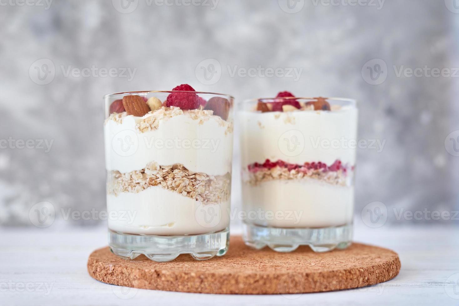 Two glasses of greek yogurt granola with raspberries, oatmeal flakes and nuts photo