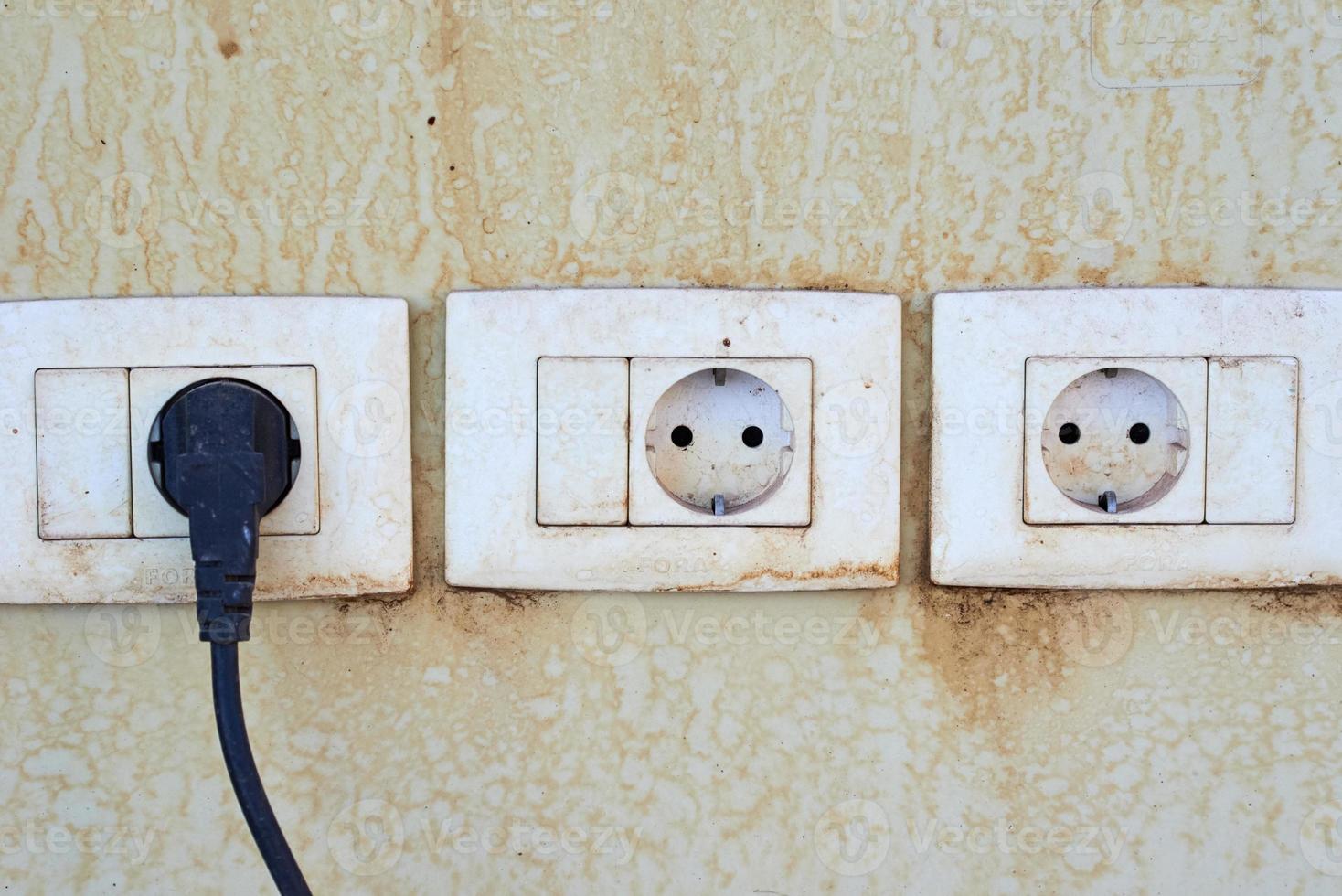 Three old damger sockets on a wall with cord cable plugged in one socket photo