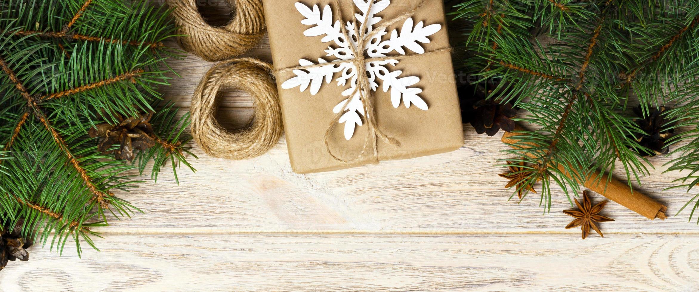 Christmas background with gift boxes wrapped in kraft paper, fir tree branches, pine cones, cinnamon and star anise on white wooden background. Flat lay, top view photo