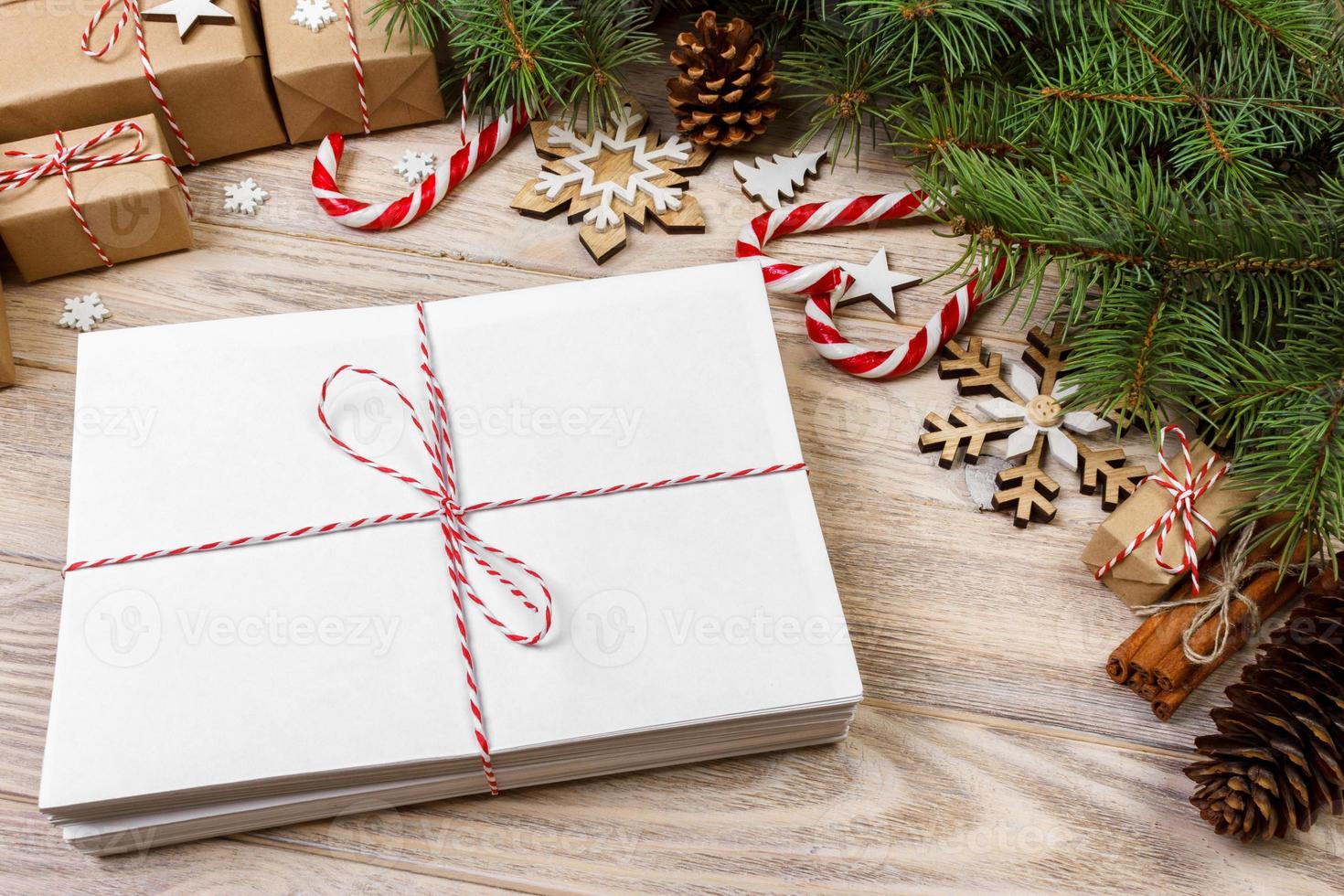 Envelope with blank sheet of paper on Christmas background - fir branch, pine cones, red ribbon, star and heart of sweets. Space for your text photo
